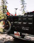 Black Cache truck bed with a bicycle attached, surrounded by trees and nature.