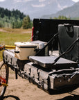 Truck bed with camping gear and a bicycle, set against a mountainous landscape.