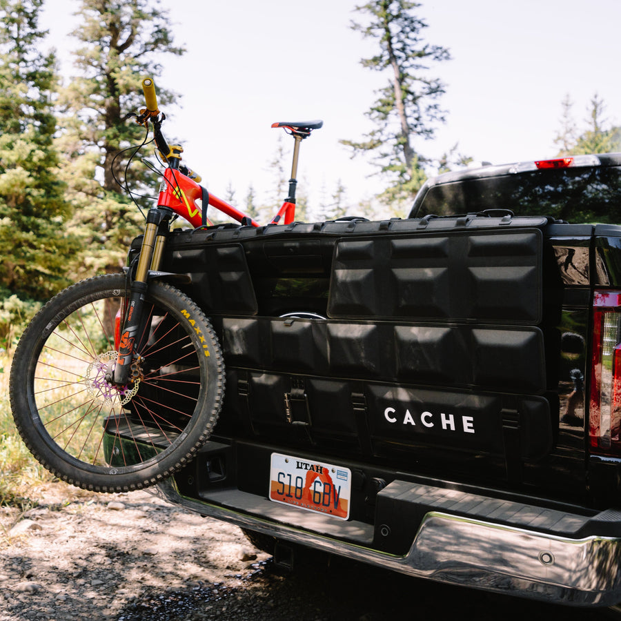 Black Cache truck bed with a bicycle attached, surrounded by trees and nature.
