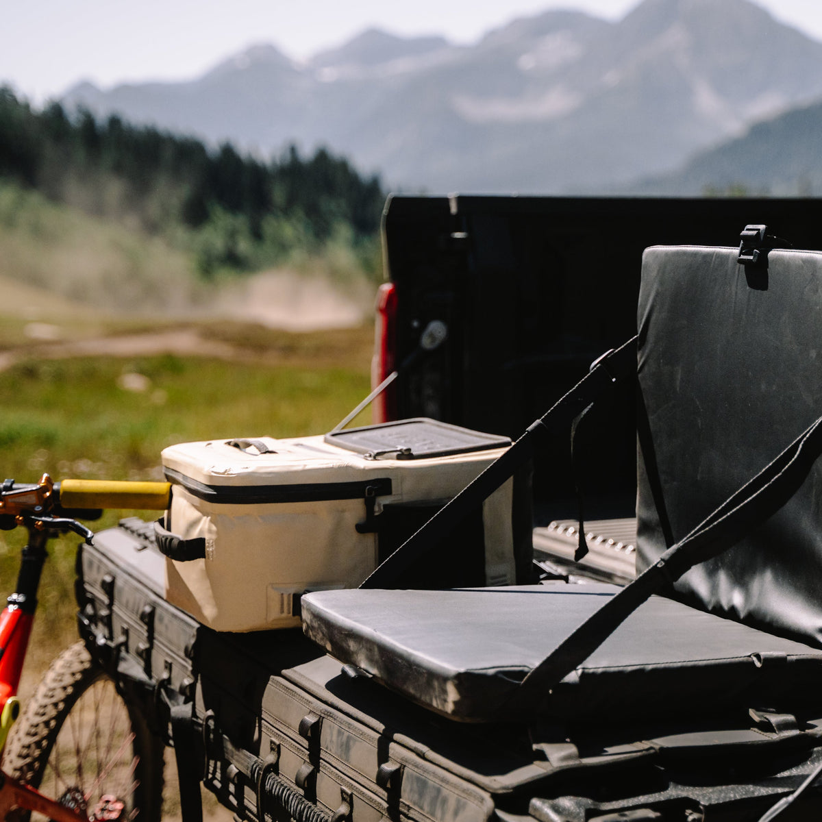 Back of a pickup truck with a cooler and chair in a mountainous landscape