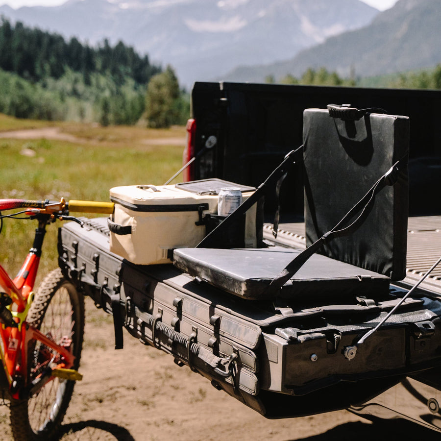 Truck bed with camping gear and a bicycle, set against a mountainous landscape.