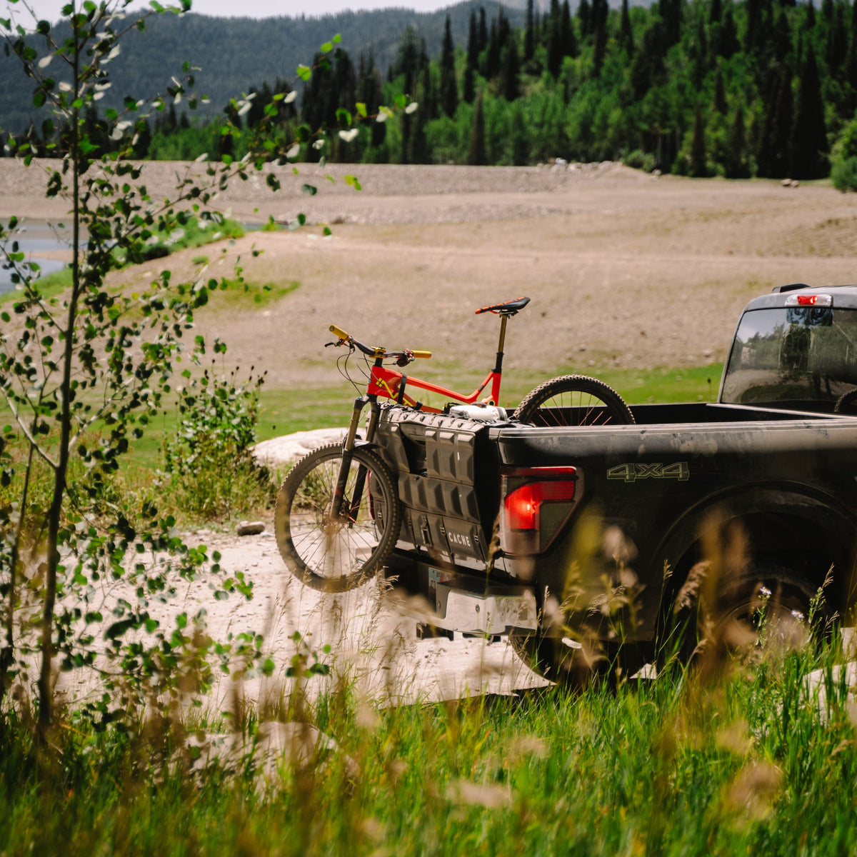 Truck with a bike in the back on a dirt road near a lake and forest.
