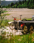 Truck with a bike in the back on a dirt road near a lake and forest.