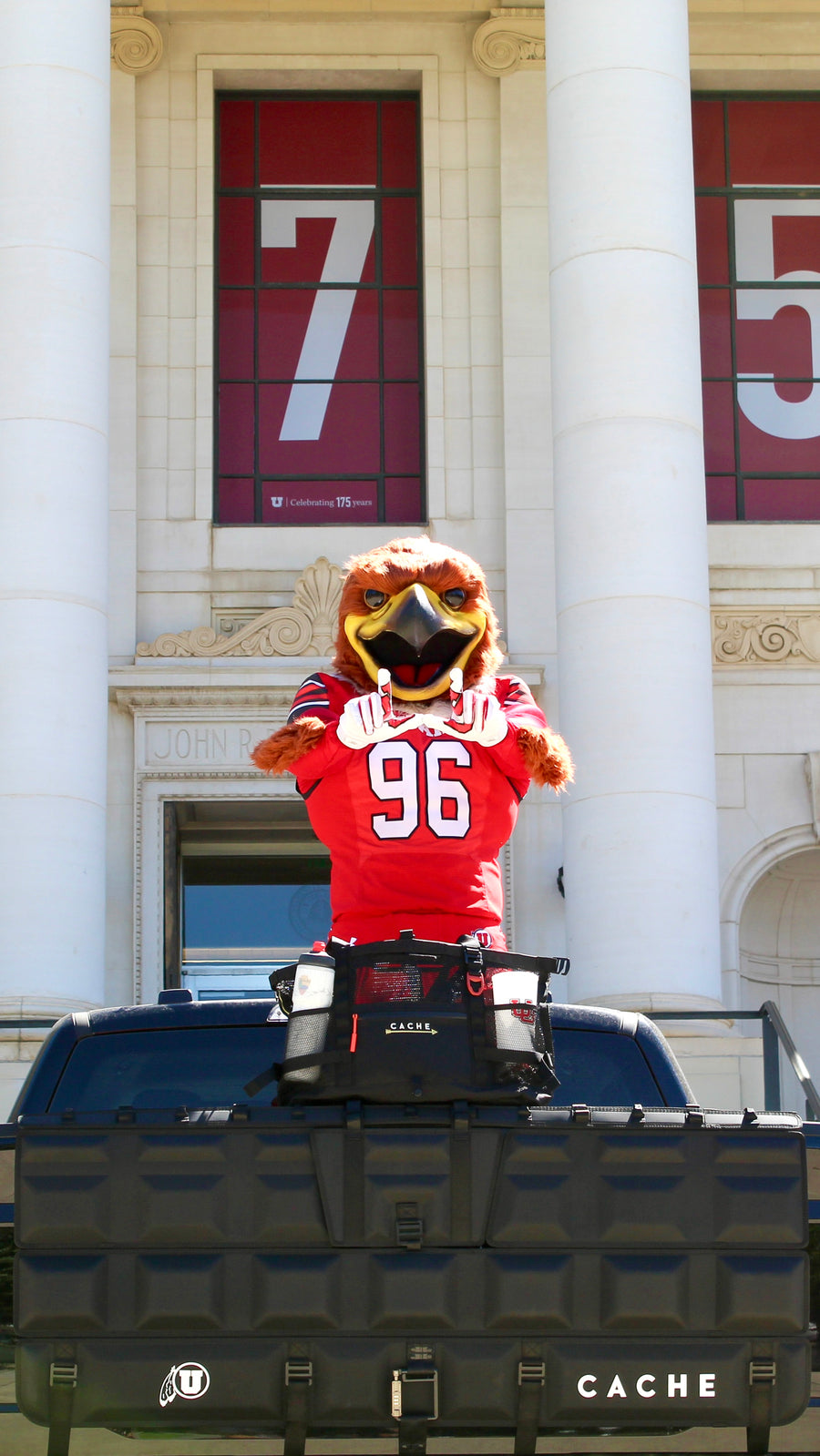 Mascot in a red jersey with number 96 on a vehicle in front of a building with large numbers.