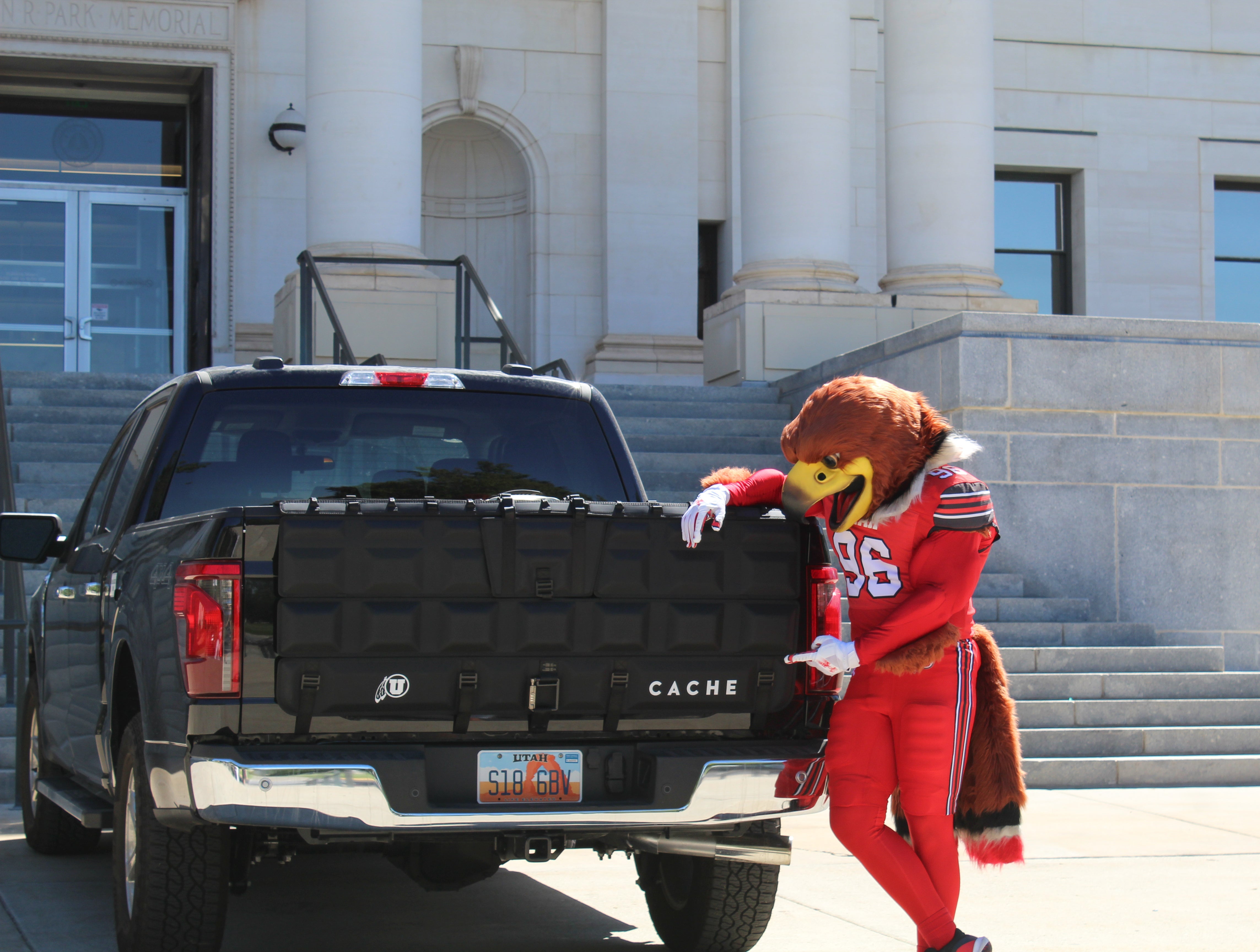 Person in a red and yellow costume leaning on a black truck with a building in the background
