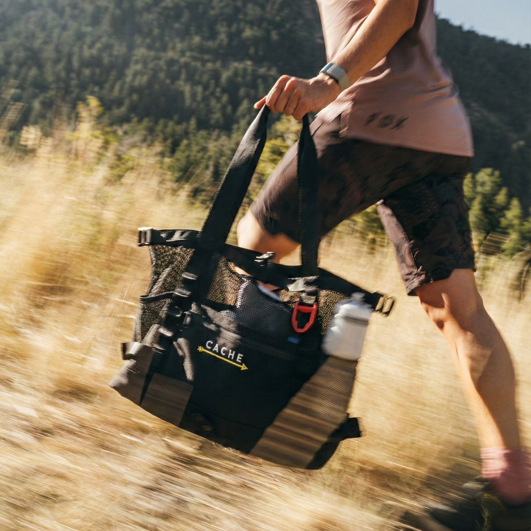 Person running outdoors with a black bag labeled 'CACHE' in a natural setting