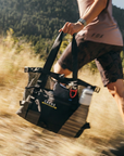 Person running outdoors with a black bag labeled 'CACHE' in a natural setting