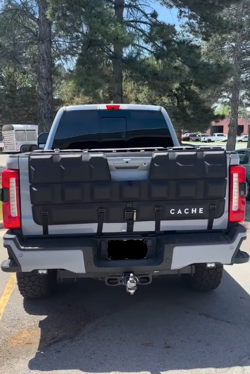 Back of a truck with 'CACHE' branding in a parking lot with trees in the background