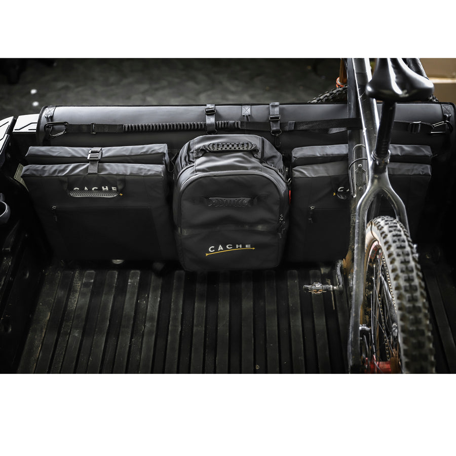 Cache Basecamp System installed in the truck bed, with a cooler and lounger chairs secured by MOLLE webbing, alongside a bike