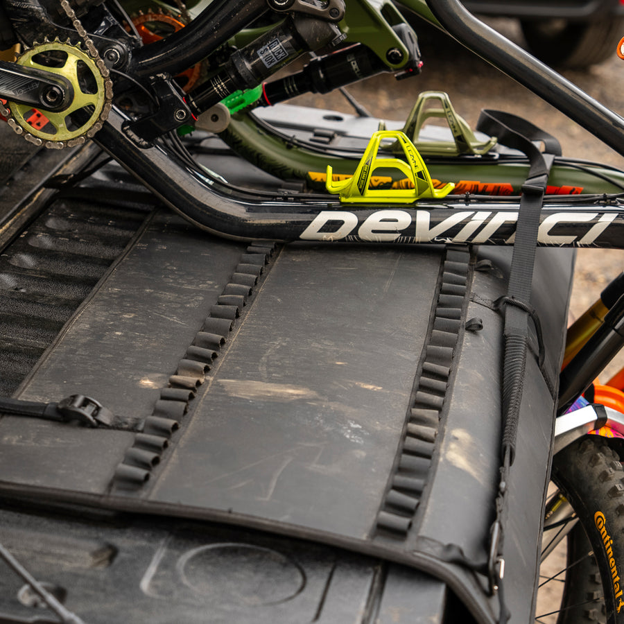 Mountain bikes secured to a tailgate pad on the back of a blue truck