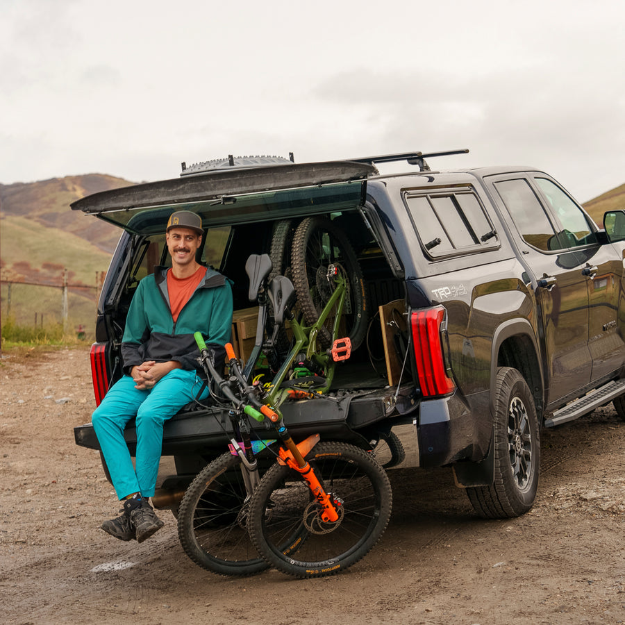 Pickup truck with padded tailgate and mountain bikes parked on a dirt road.